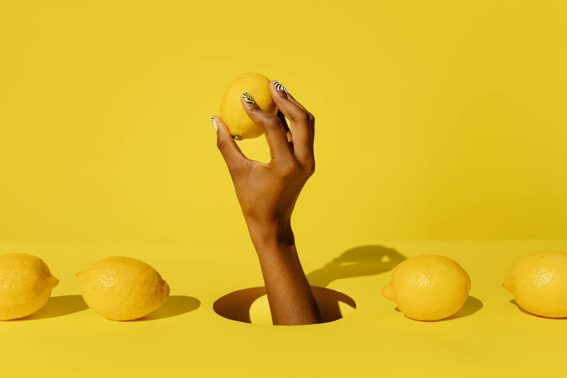 Hand holding a fresh lemon against a bright yellow background, symbolizing renewal and new beginnings