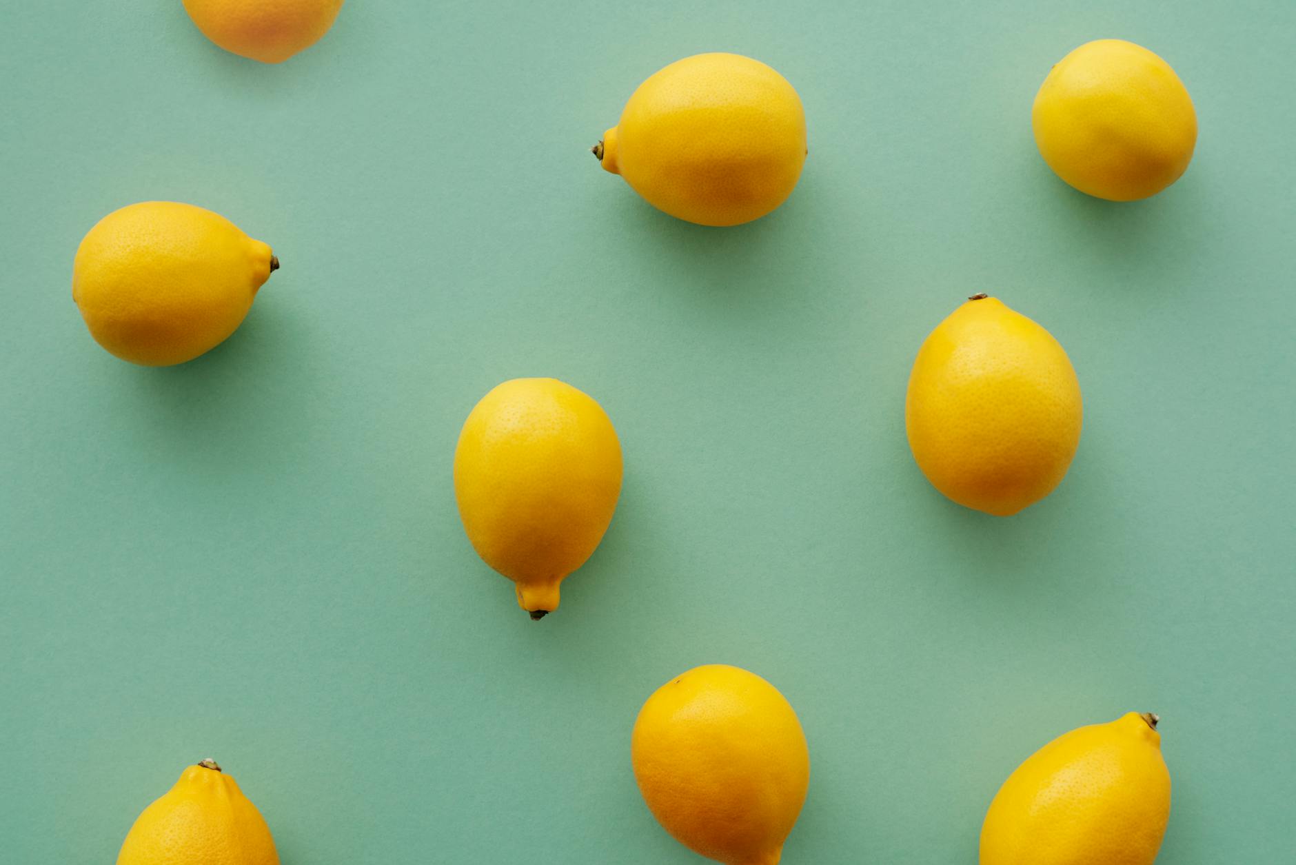 Yellow lemon clitoral vibrator surrounded by fresh lemons on a bright yellow background