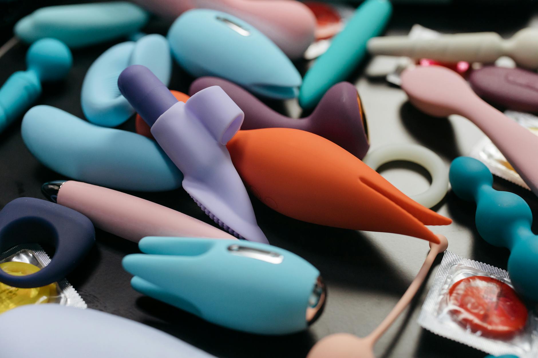 Two hands gently holding pink and blue silicone vibrators against a soft pastel background