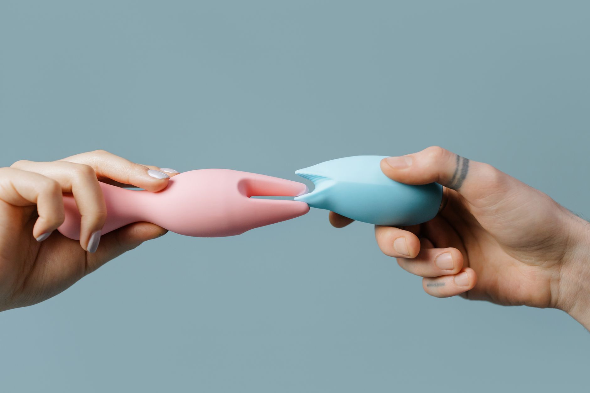 Hands holding colorful silicone vibrators, showing pleasure toy options