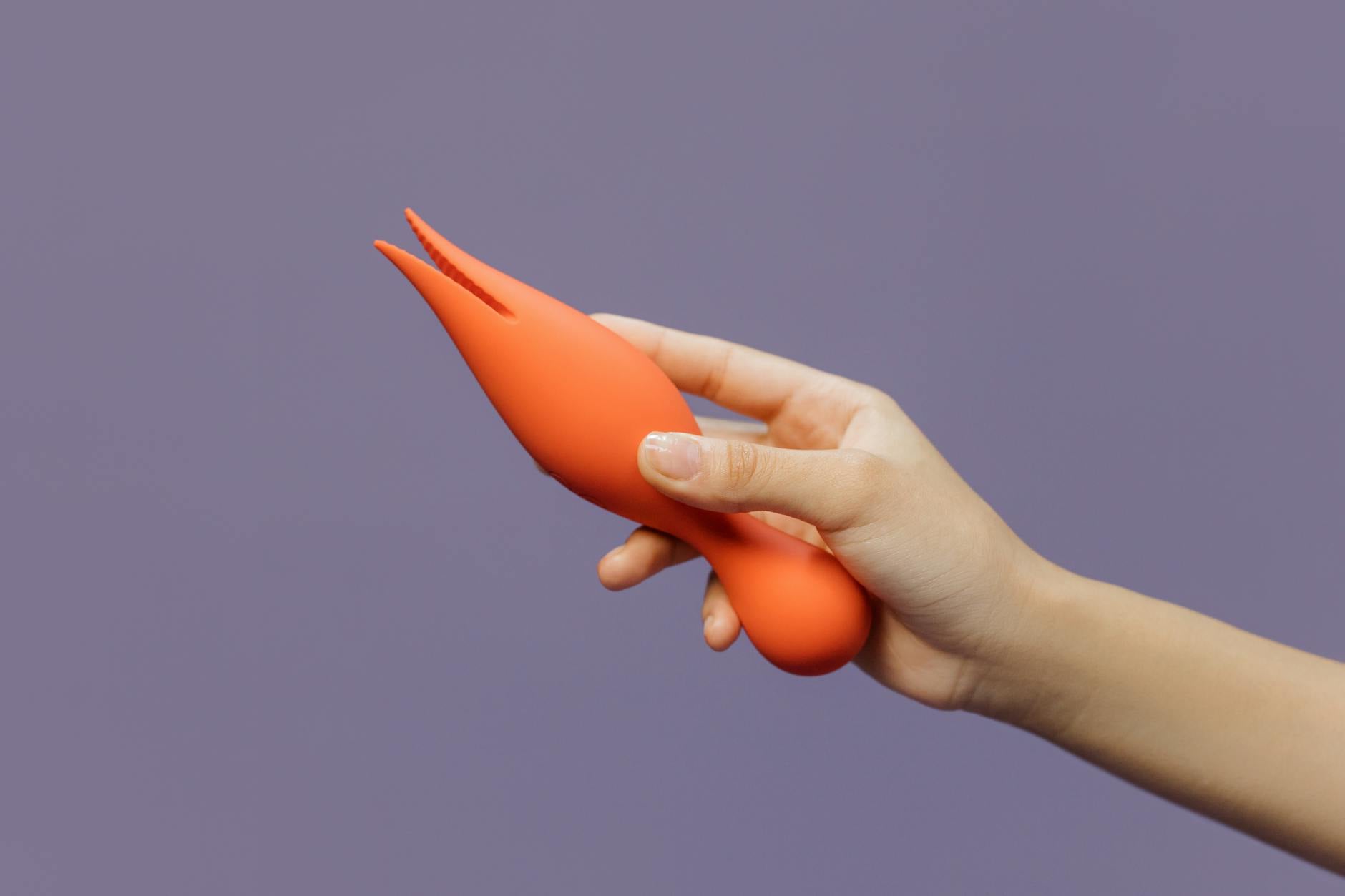 A close-up of a hand holding a lemon vibrator against a minimalistic purple backdrop.