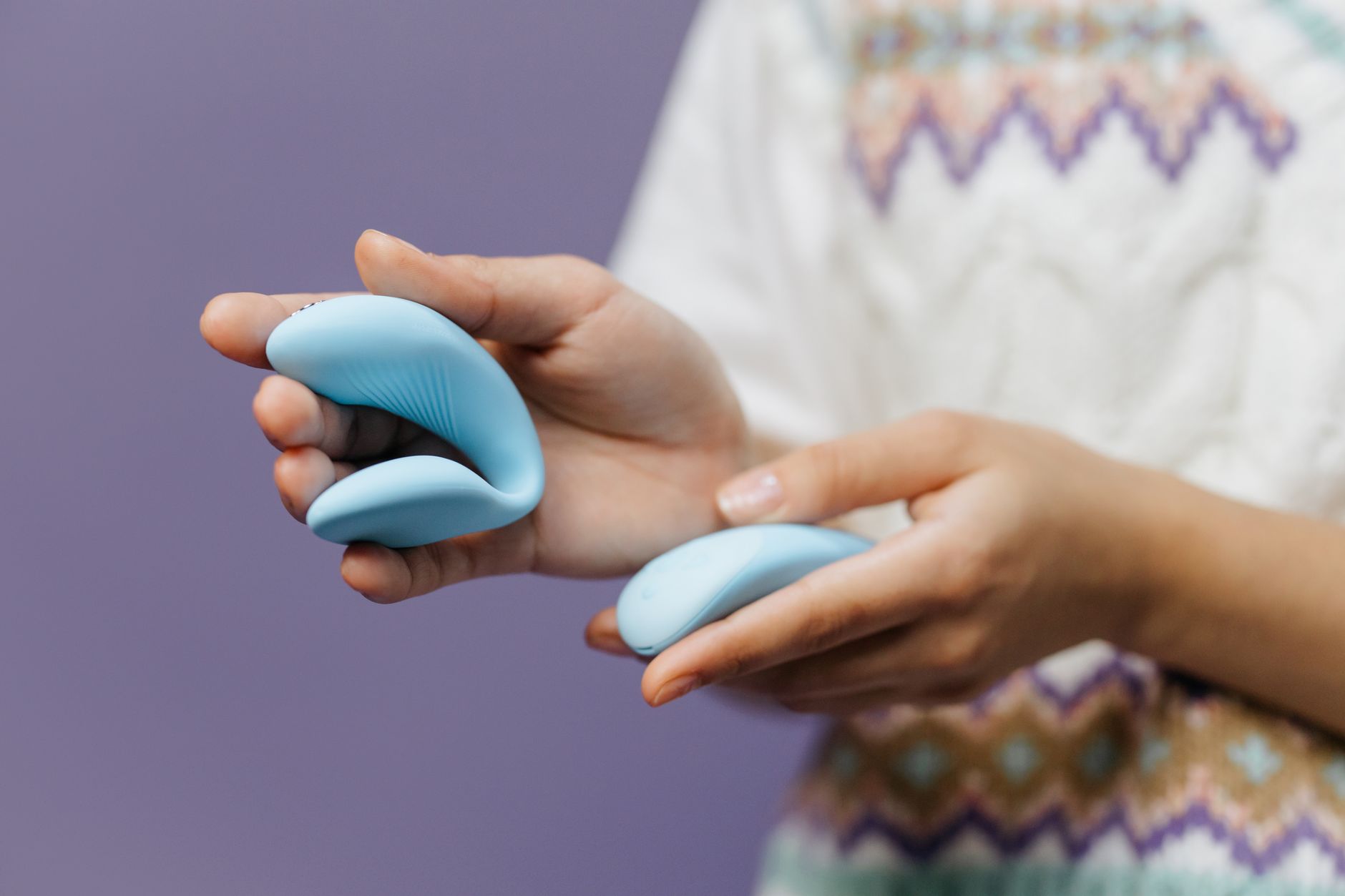 Hands holding a sleek clitoral vibrator against a purple background, representing intimate pleasure tools for mature bodies.