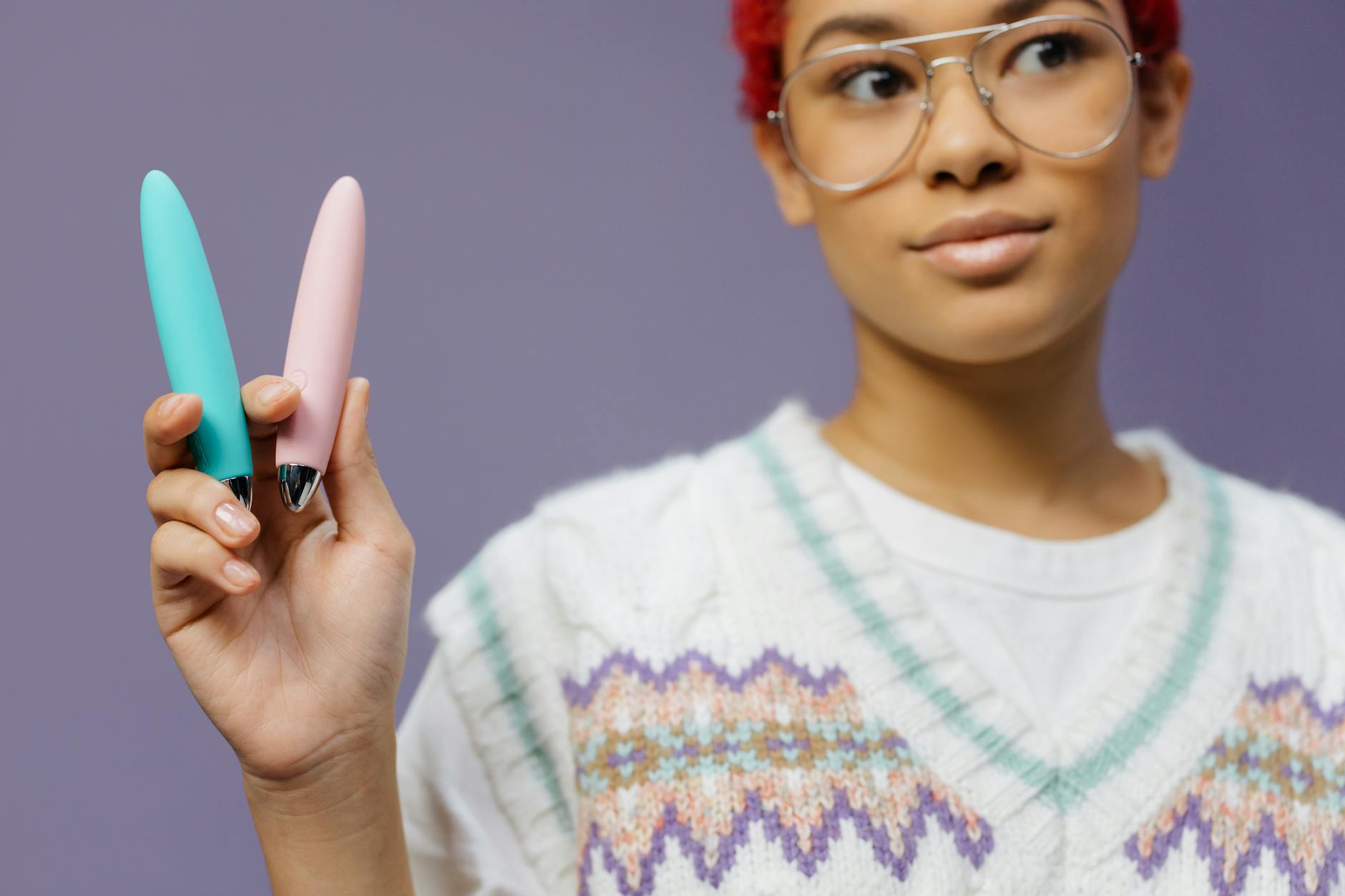 Woman holding vibrators against a purple background, representing different pleasure techniques