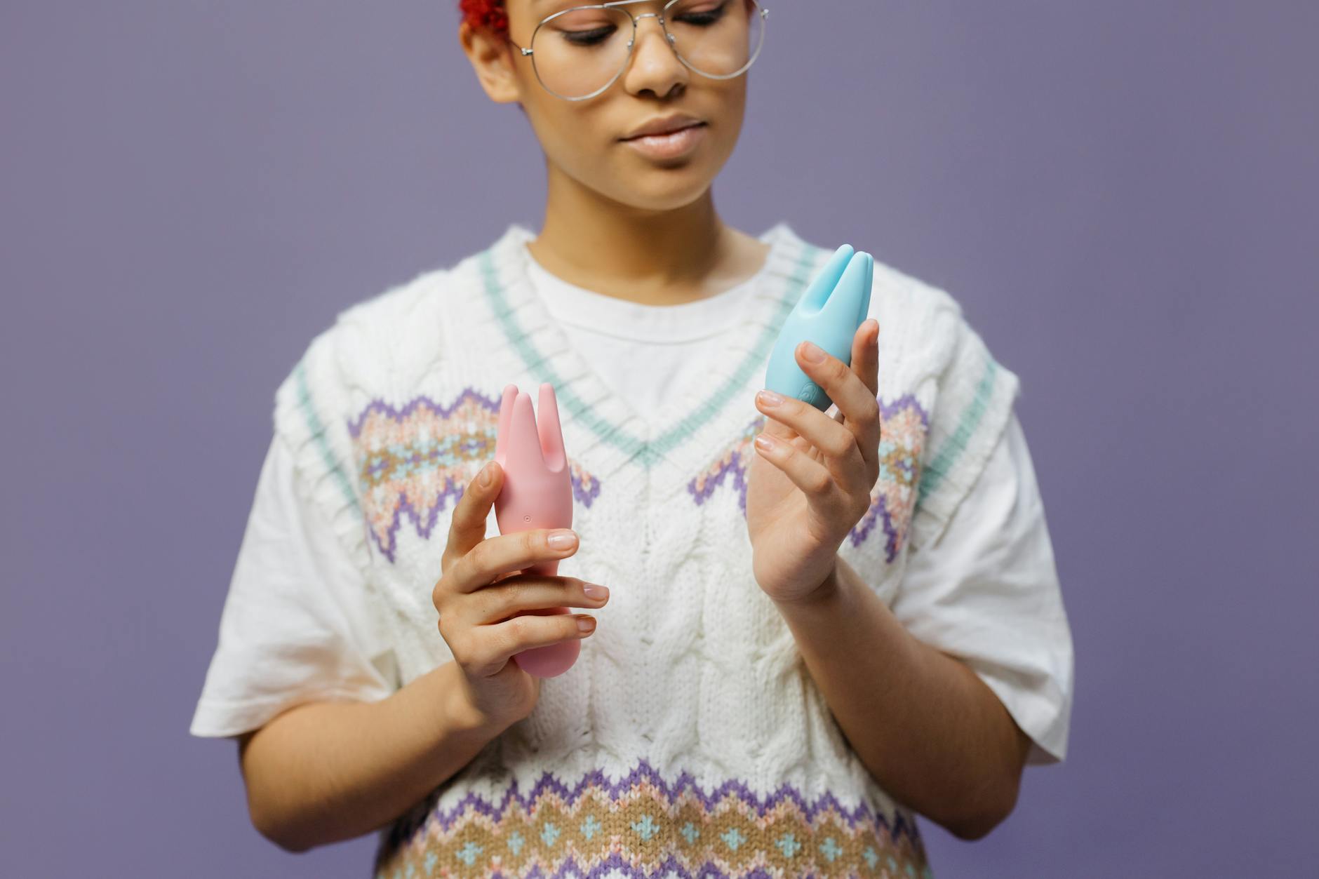 Woman holding blue and pink silicone vibrators while considering how hormonal changes affect sensation and pleasure.