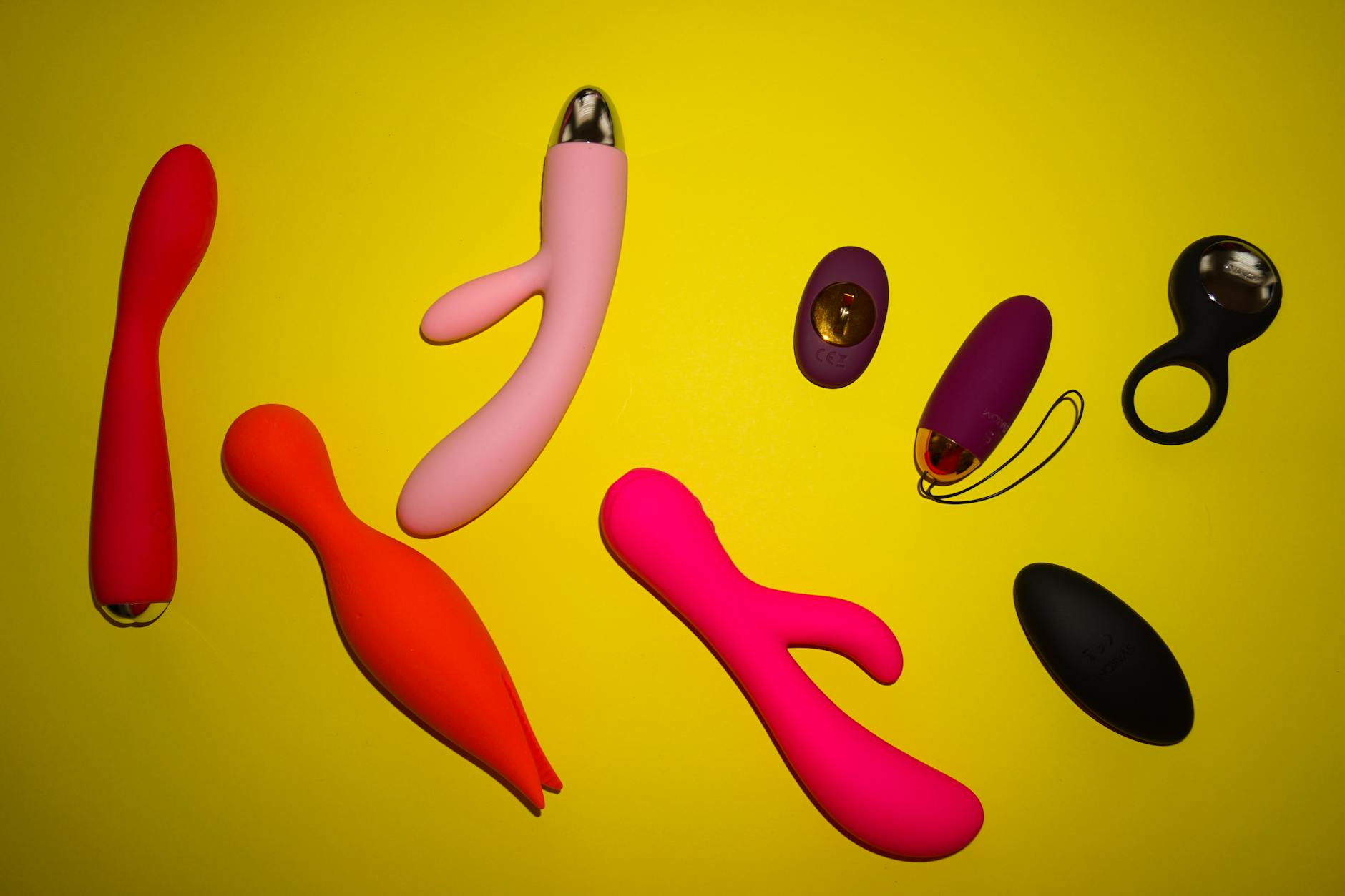 Assortment of colorful vibrators and clitoral toys on a bright yellow surface